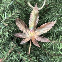 Copper hemp leaf ornament on pine tree background.