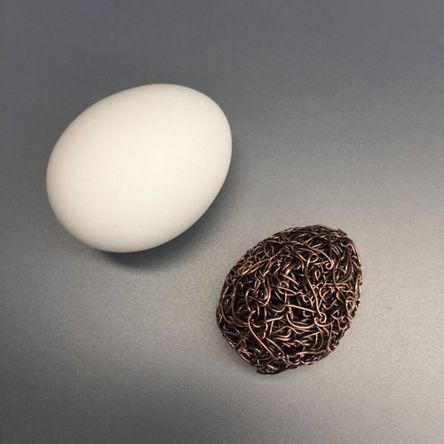 woven copper egg next to real egg